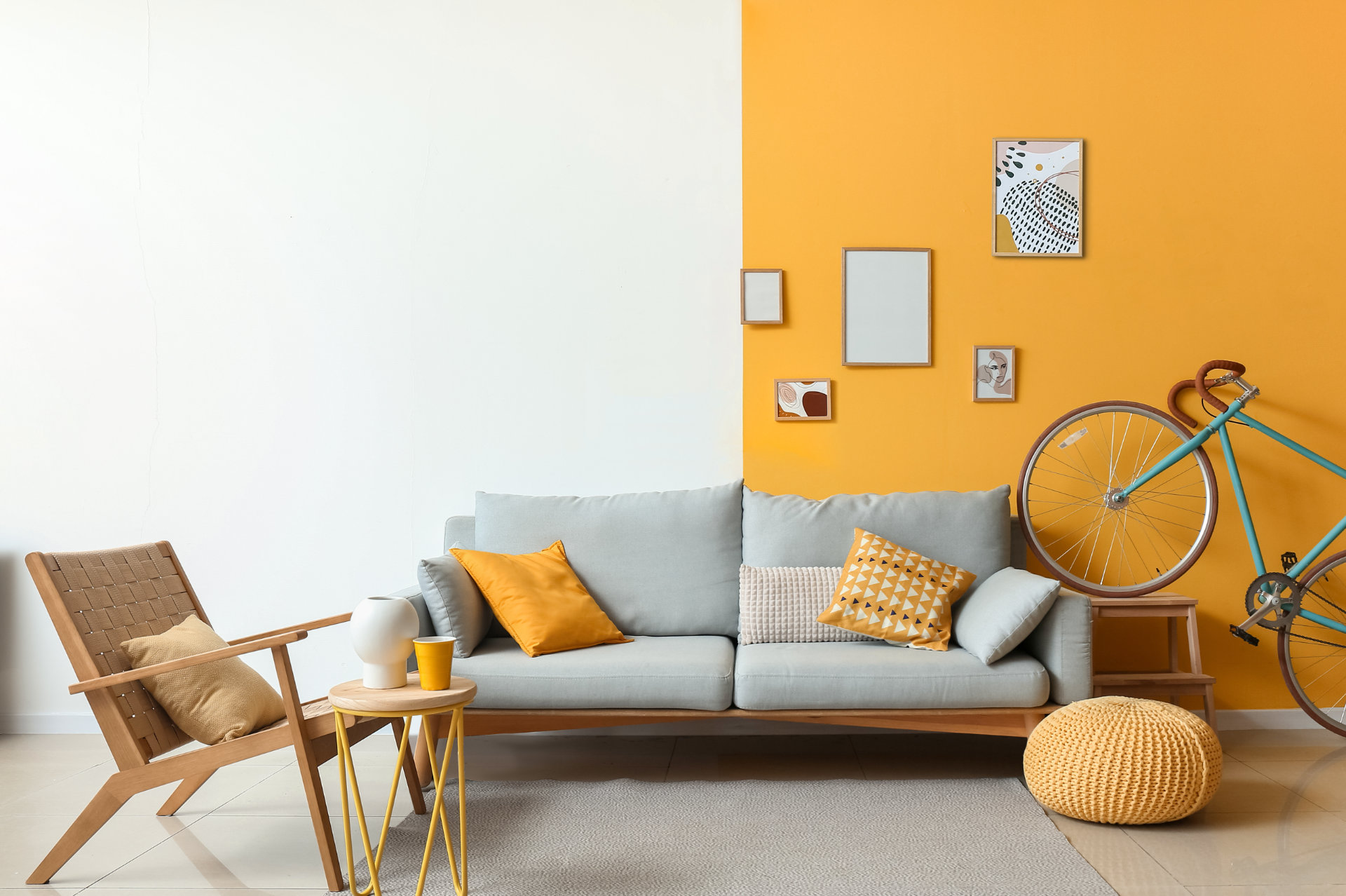 Photo d'un intérieur coloré avec un canapé, une chaise, une table d'appoint et un vélo devant un mur. Le mur est blanc à gauche et peint en jaune foncé à droite - ArchiBienPensé, architecte d'intérieur à Annecy